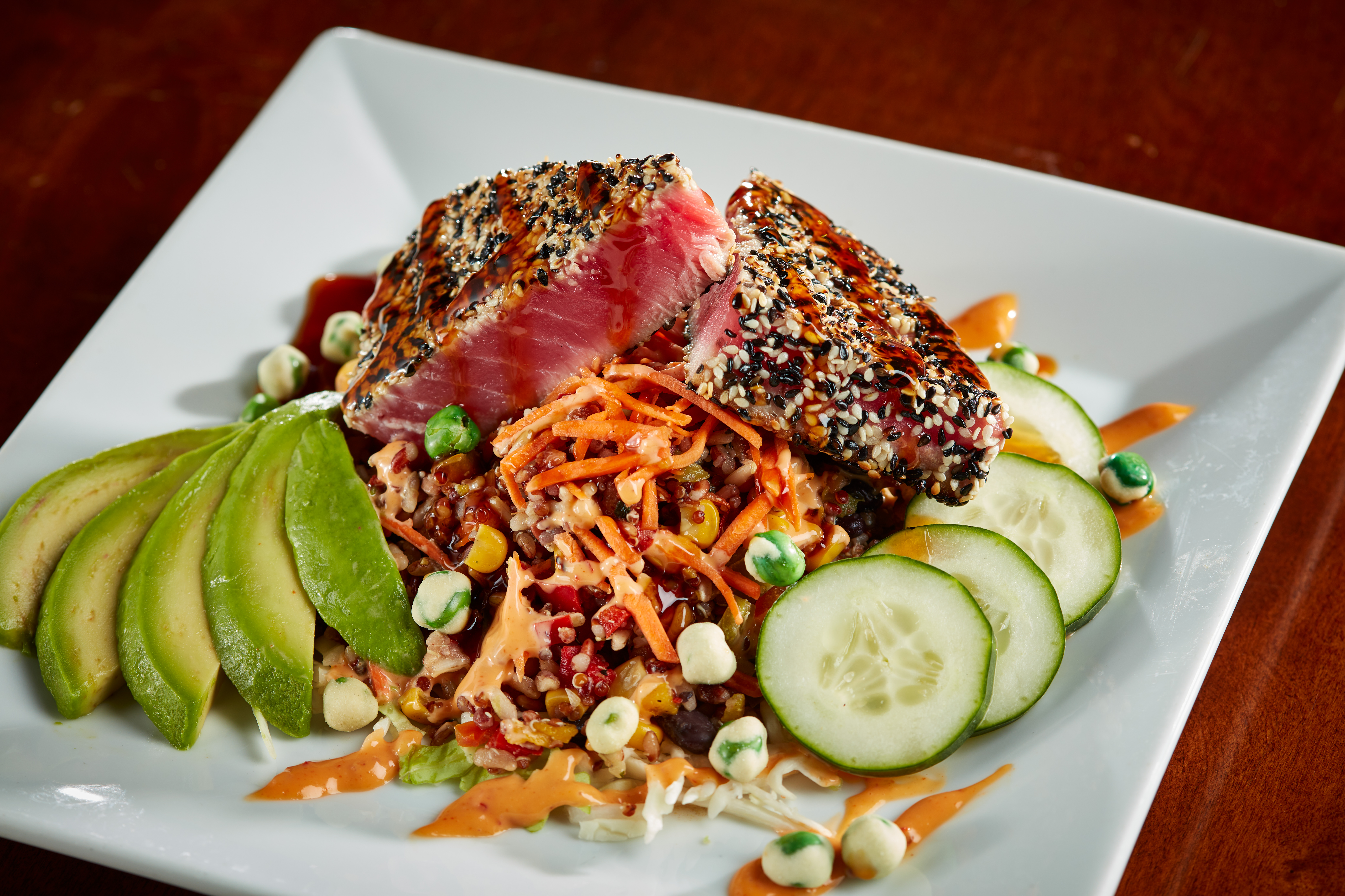 Seared sesame crusted tuna over shredded cabbage and fire-roasted grains, topped with bang-bang sauce. Garnished with sliced cucumber, avocado, a teriyaki glaze and wasabi peas. $18.99