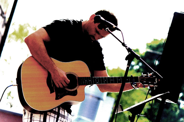 Chad Demeuse playing the guitar in front of a microphone